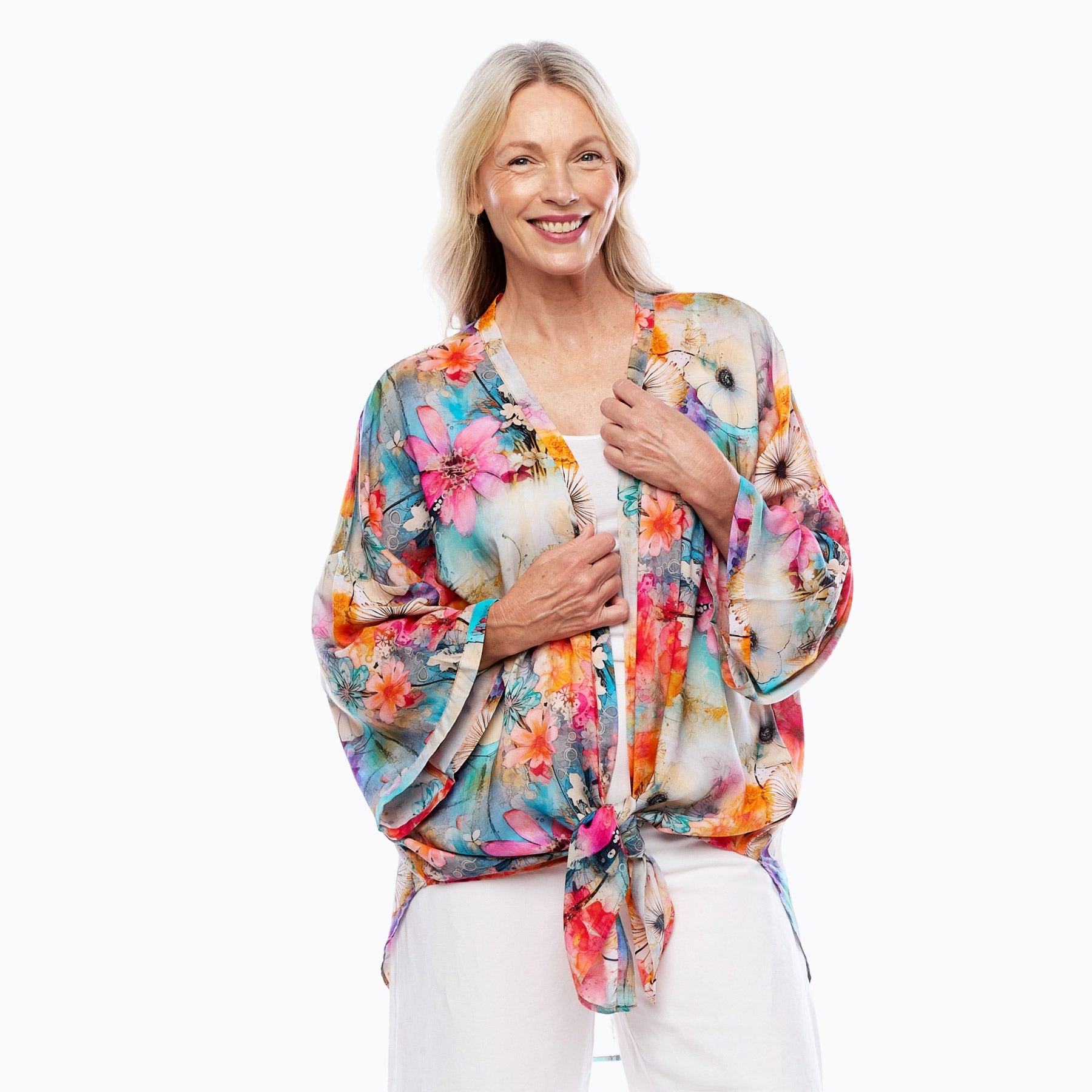 Woman wearing a colorful floral kimono top by Claire Powell, styled with white pants