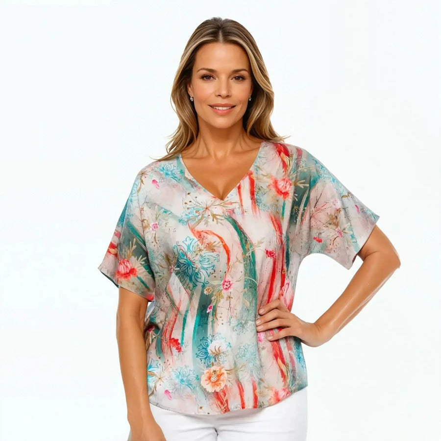 Woman wearing a Claire Powell floral V-neck T-shirt in meadow print, styled with white pants