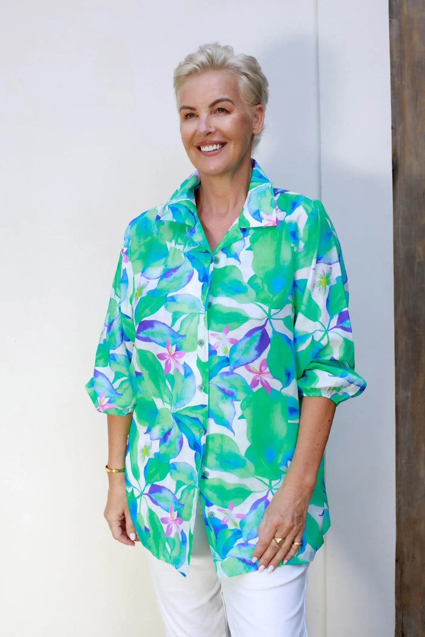 Woman wearing a green floral print Claire Powell shirt and white pants, smiling