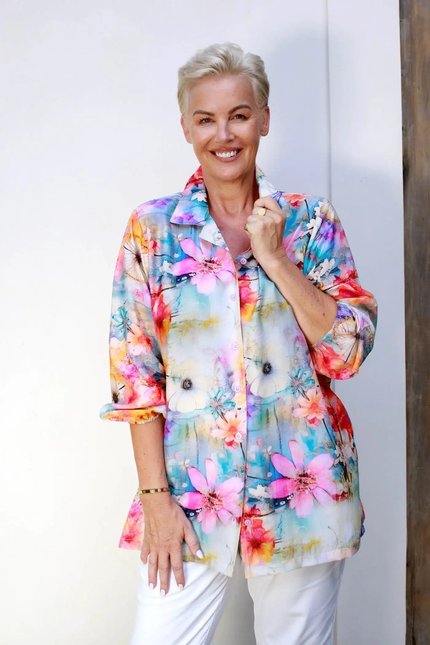 Woman wearing a colorful floral button-up shirt from Claire Powell, smiling against a white wall.