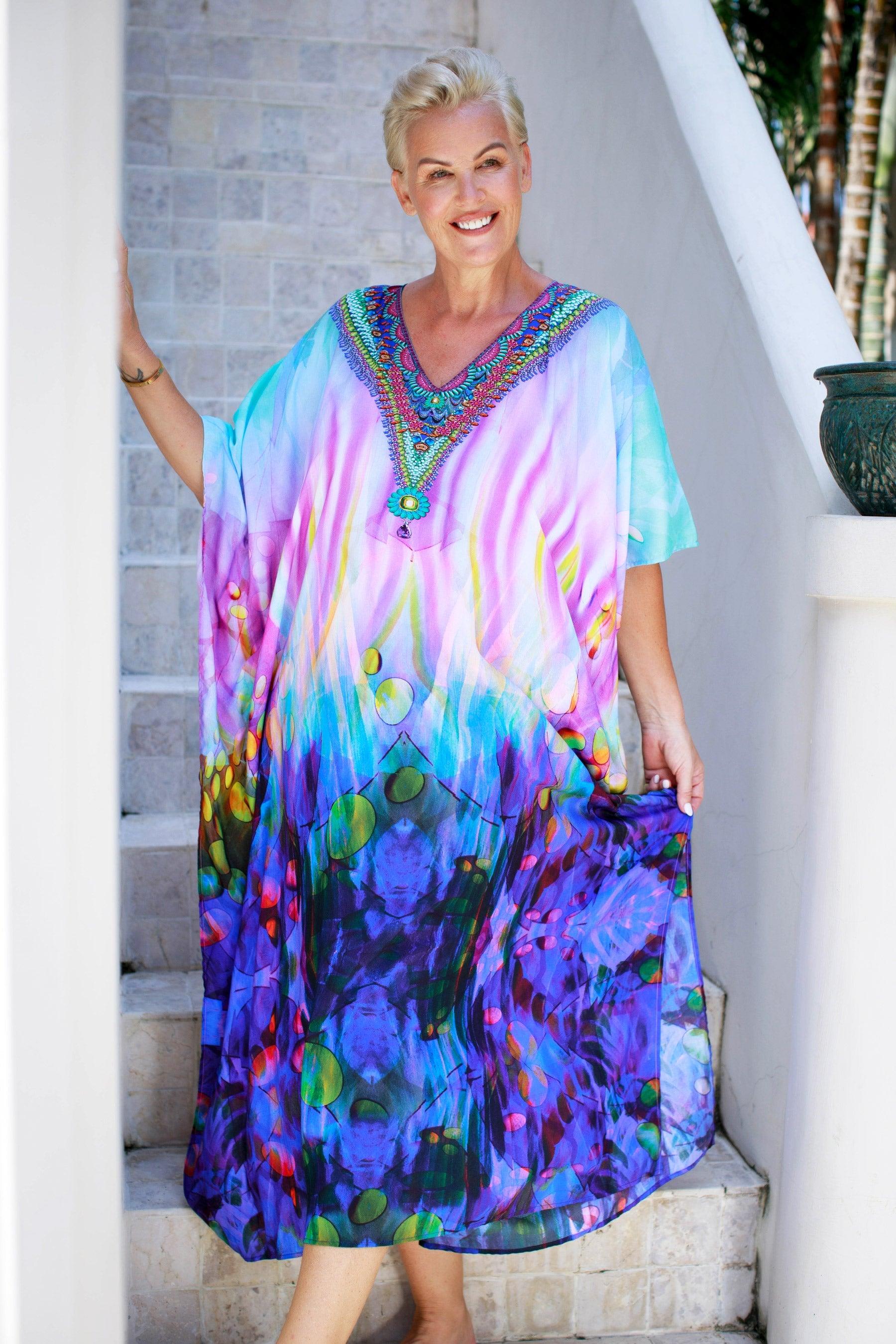 Woman wearing a colorful, flowy Claire Powell kaftan, smiling on a staircase outdoors.
