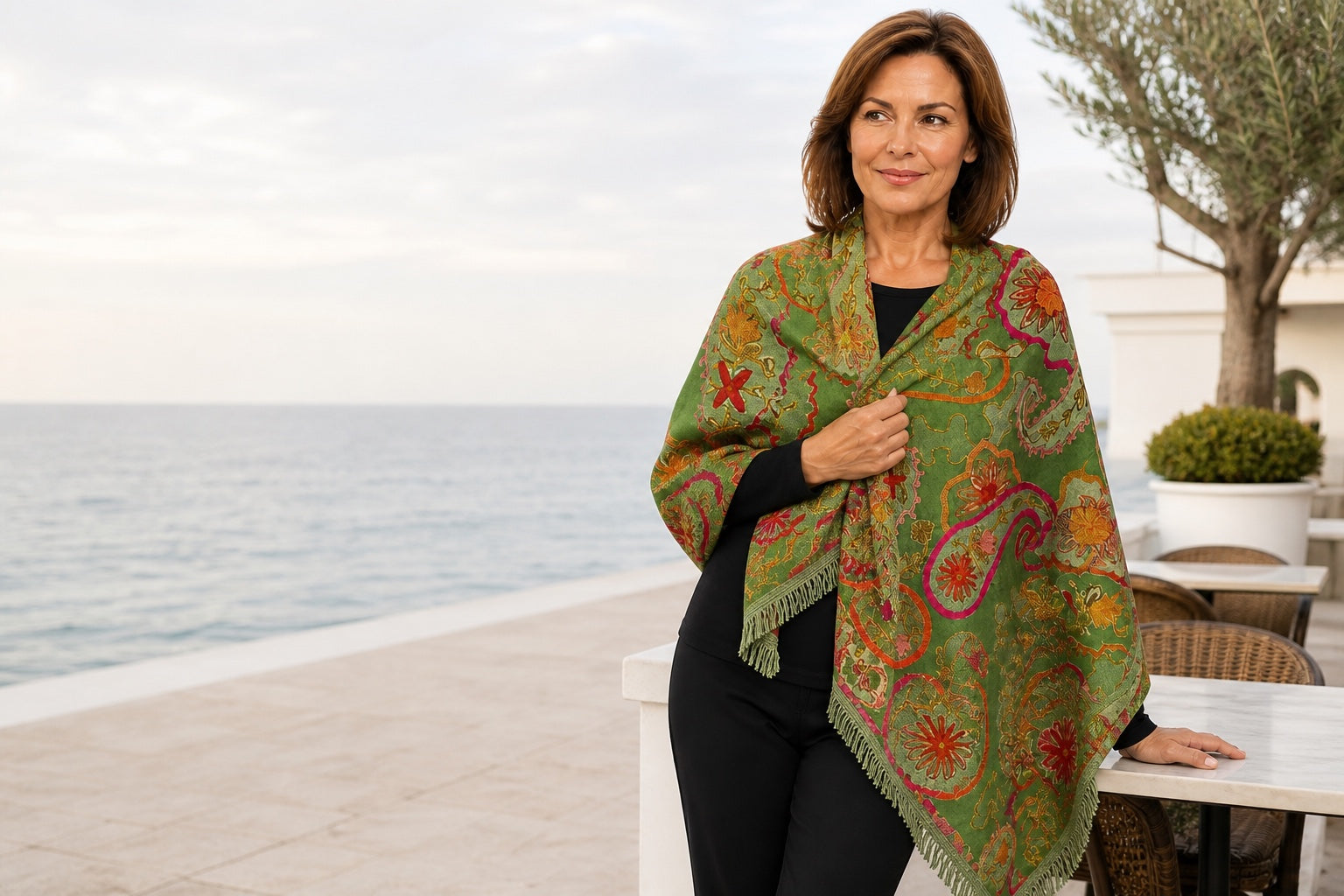 Woman styling the embroidered Olive wool shawl at a coastal cafe