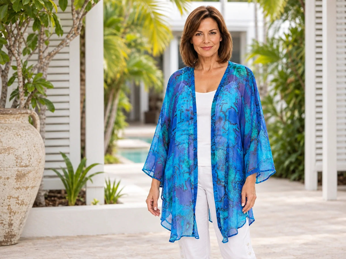Woman wearing the Claire Powell Reef cotton chiffon kimono over a white camisole and white capri pants in a tropical resort courtyard