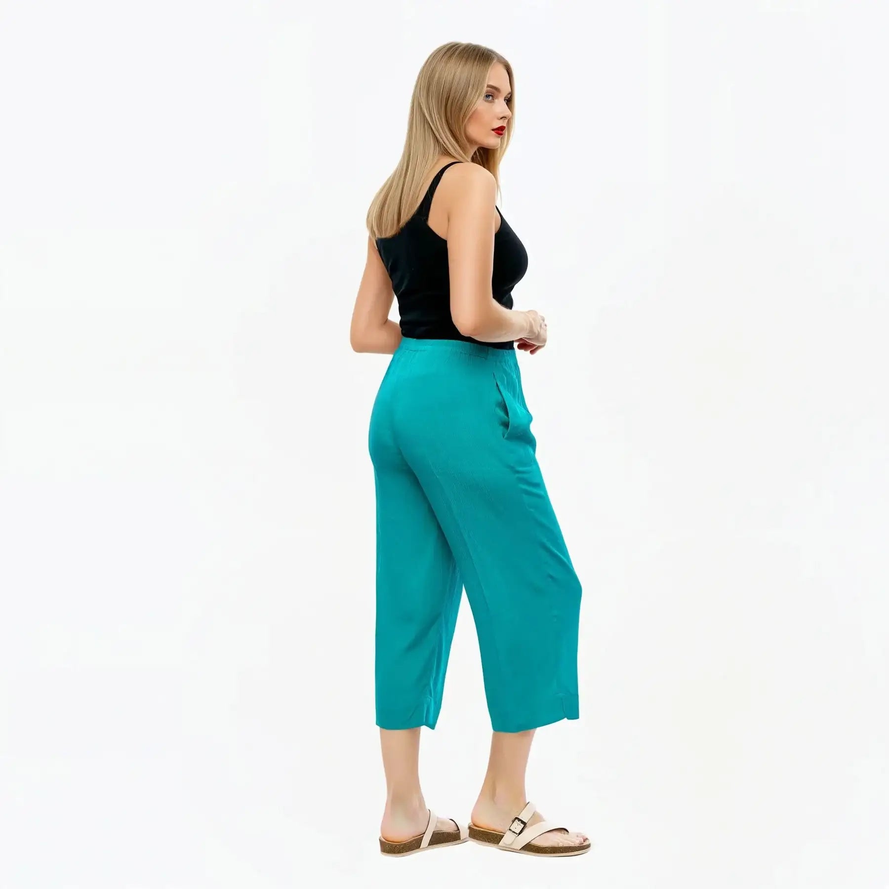 Woman wearing teal pants and a black top on a white background