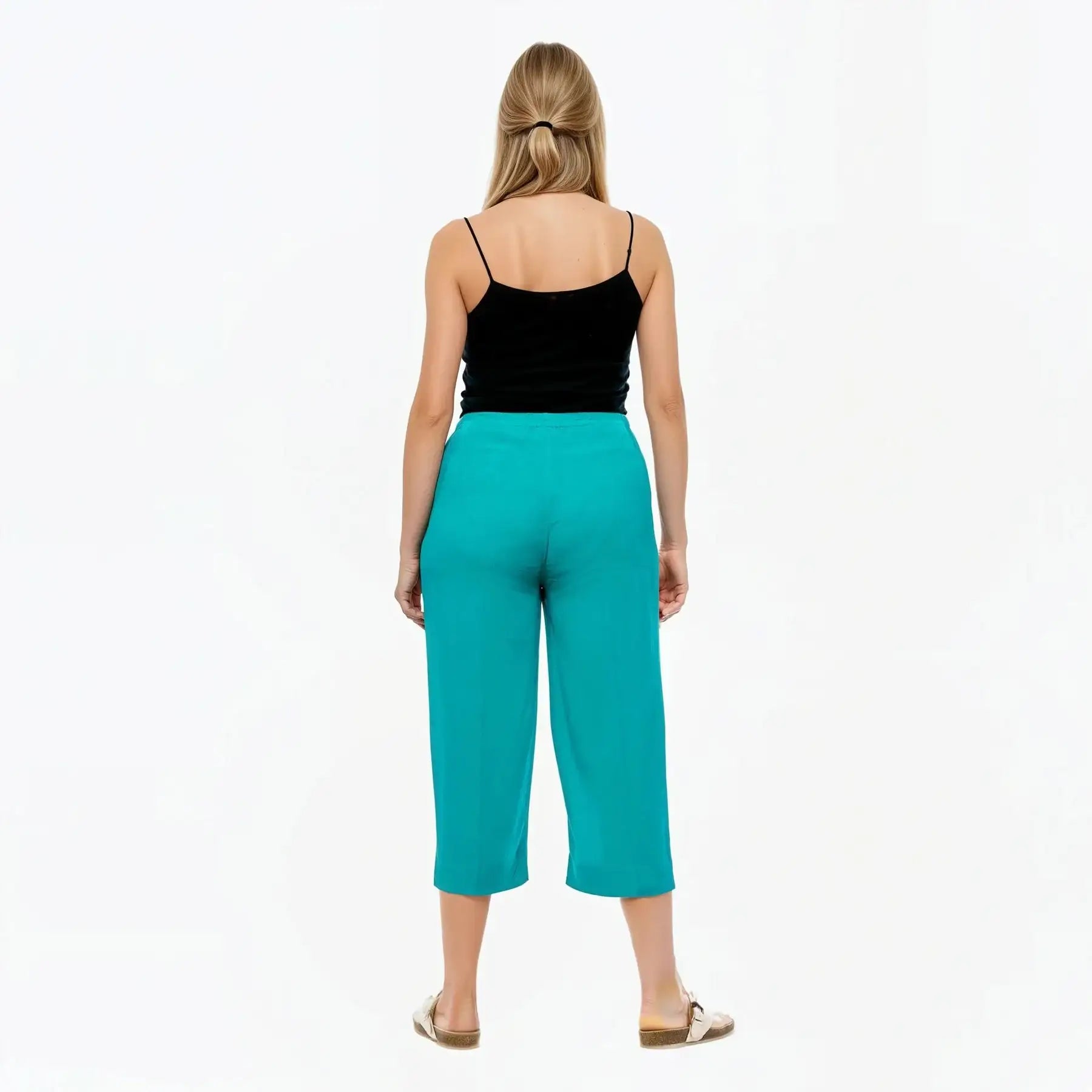 Woman wearing teal capri pants and a black top on a white background