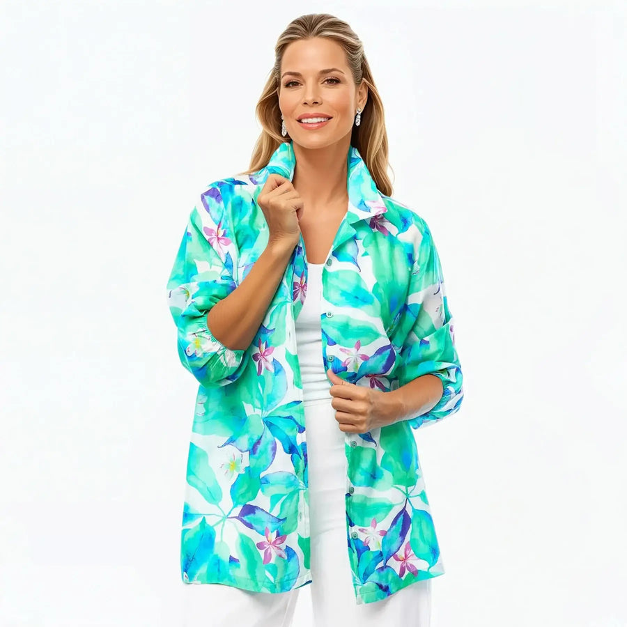 Woman wearing a green floral collared silk shirt by Claire Powell, styled with white pants