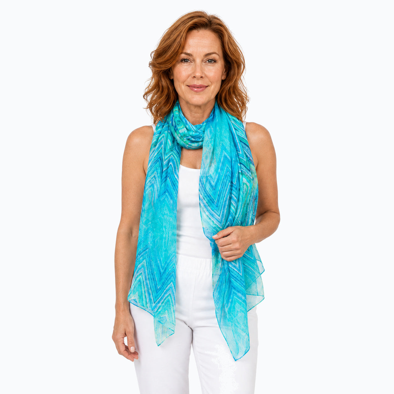 Woman wearing the Claire Powell Serenity silk scarf, looped around the neck with long hanging ends, white camisole and white capris