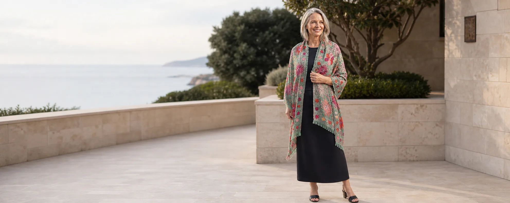 Mature model wearing the Claire Powell Sage embroidered wool shawl at a coastal resort
