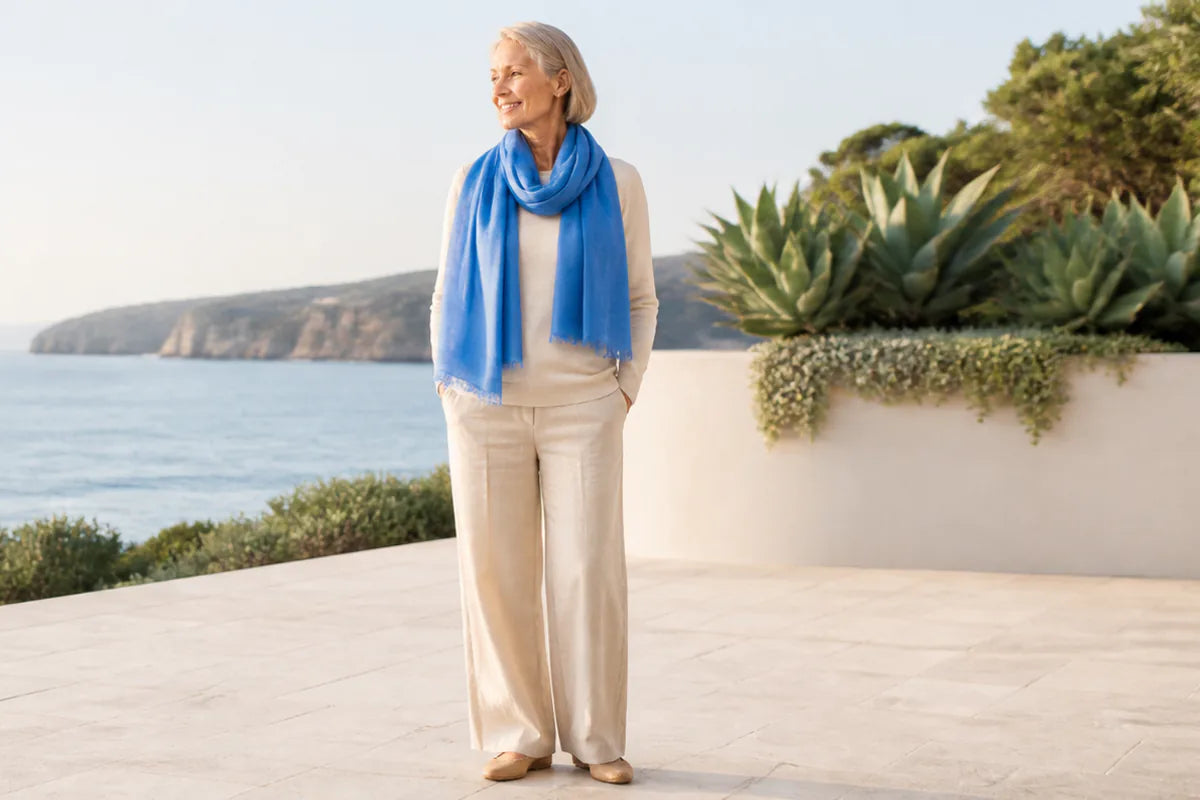 Mature model wearing the Claire Powell Denim Blue silk-wool scarf at a coastal resort