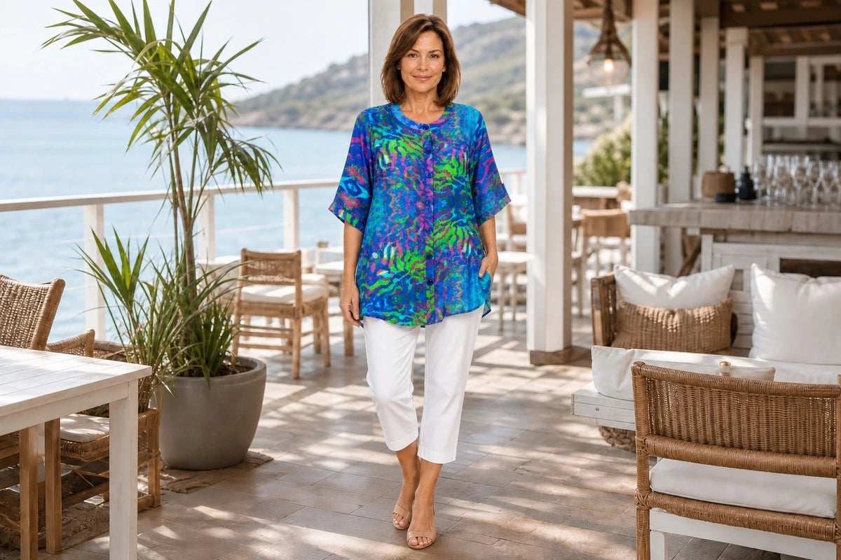 Mature model wearing the Claire Powell Mirage A-Line Tunic Shirt with white cotton-lycra capri pants at a coastal resort