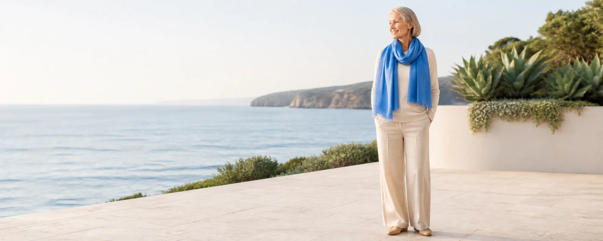 Mature model wearing the Claire Powell Denim Blue silk-wool scarf at a coastal resort